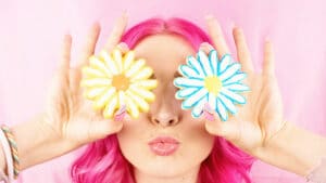 Fille aux cheveux roses avec des gateaux en forme de fleur devant les yeux